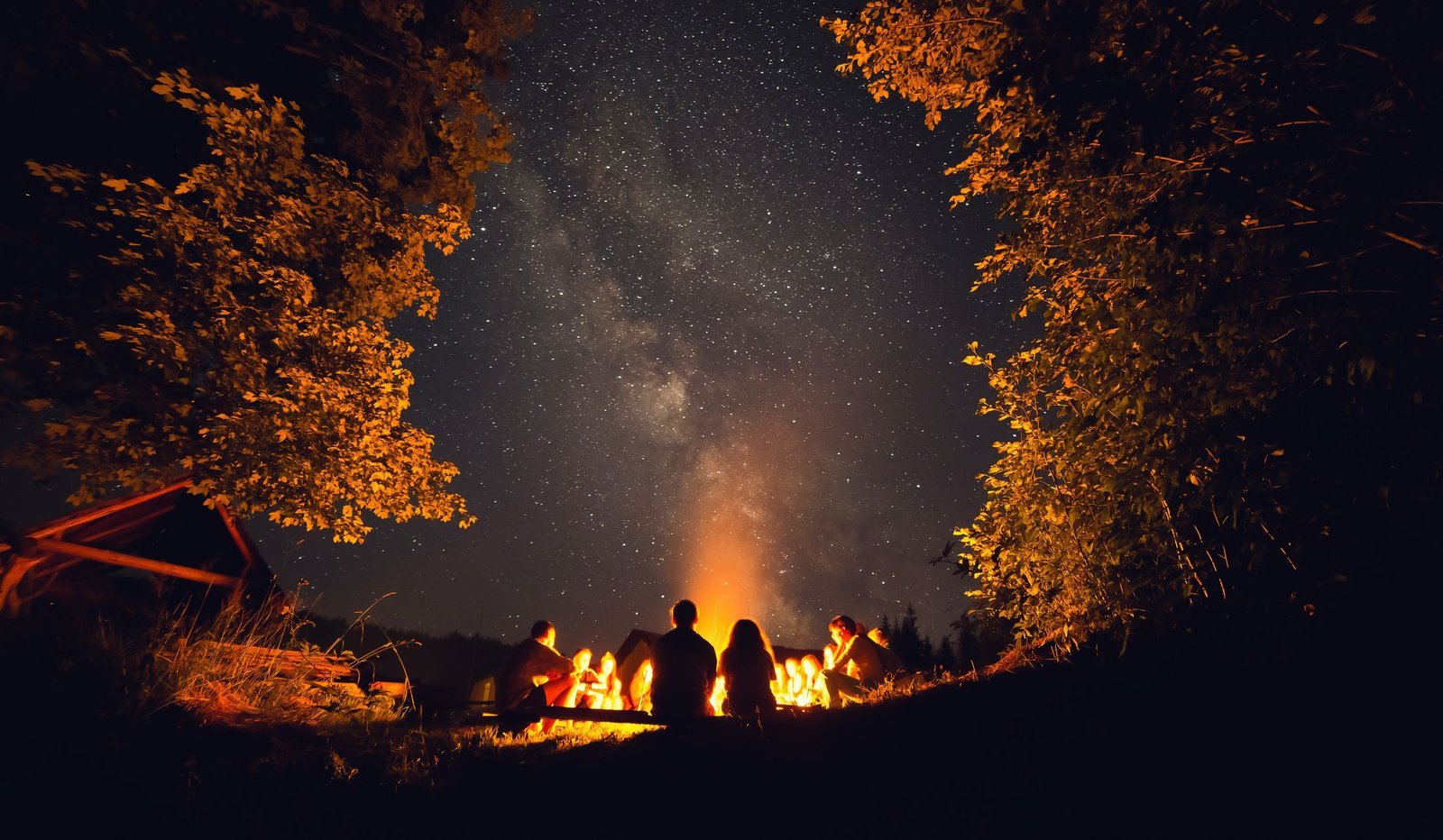 People gathered around a campfire at night beneath the Milky Way