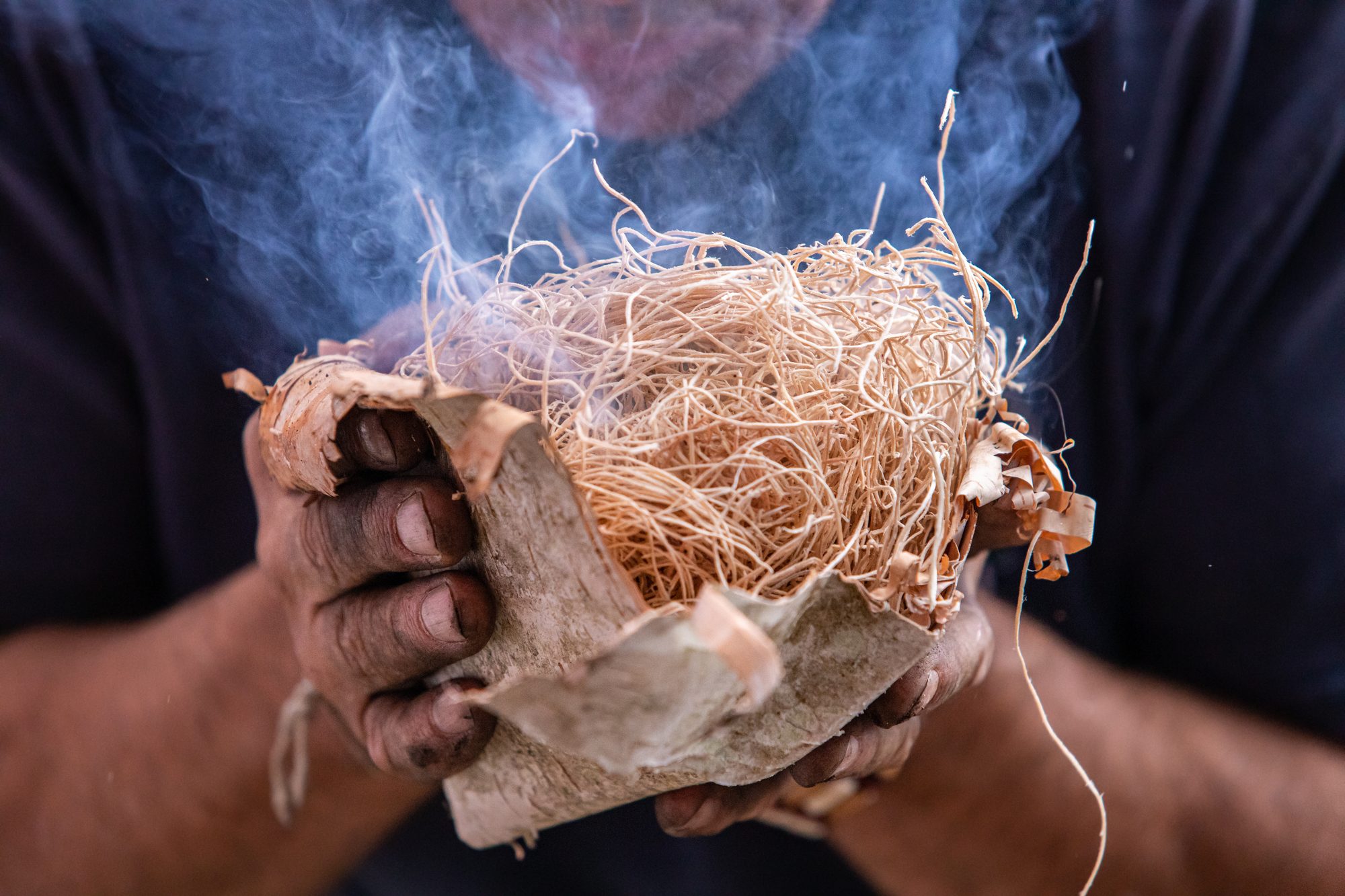 Hands holding a smoking birch-bark tinder bundle